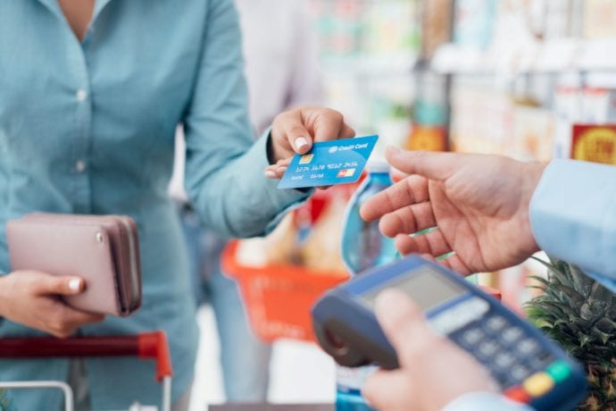 Woman hands credit card to cashier at a retail register.